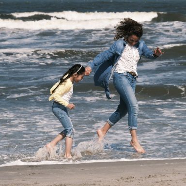 Een moeder en dochter rennen lachend door het water op het strand.