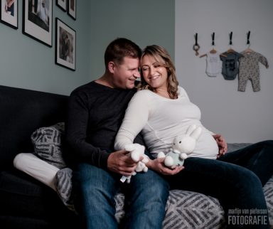 Zwangere vrouw en man zitten samen op de bank met knuffels in hun handen.
