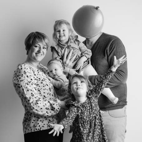 Een gezin met vier kinderen en een volwassene, met een ballon voor het hoofd van de man.