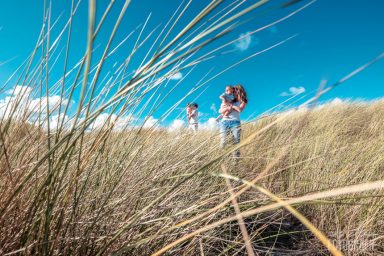 Twee mensen lopen door hoge grassprieten onder een heldere blauwe lucht.