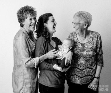 Drie vrouwen lachen samen met een baby in een woonkamer setting.