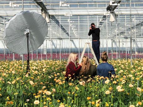 Fotografie van een modelshoot in een kas met bloemen en een fotograaf op een ladder.
