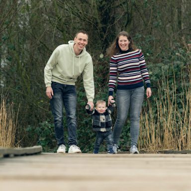Een jonge familie wandelt samen op een houten pad in de natuur.