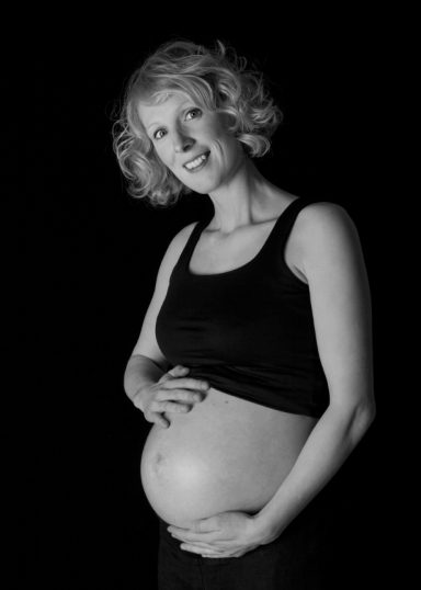 Een glimlachende zwangere vrouw met een blote buik, gekleed in een zwarte top.