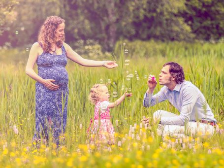 Zwangere vrouw met kind in een veld, man blaast bellen.