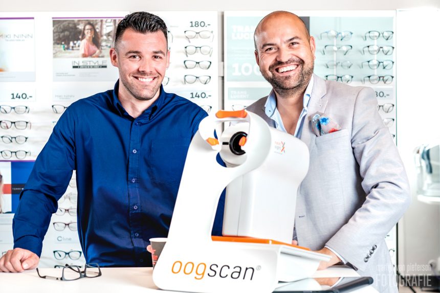 Twee mannen staan naast een apparaat voor optische scans met brillen op de achtergrond.