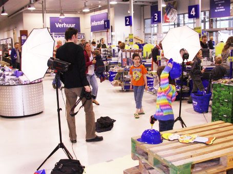 Een drukke winkel met mensen, camera's en kinderen in kleurrijke kleding.
