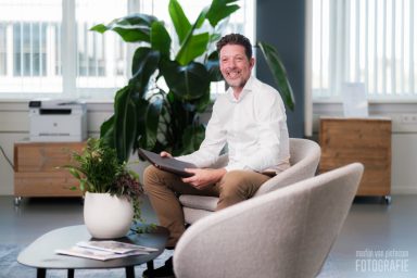 Een man in een witte blouse zit ontspannen in een moderne kantooromgeving.