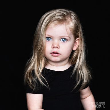 Een jong meisje met lang, blond haar en heldere blauwe ogen kijkt recht in de camera.