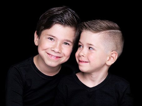 Twee jonge jongens met zwart haar, gekleed in zwarte shirts, lachen naar elkaar.