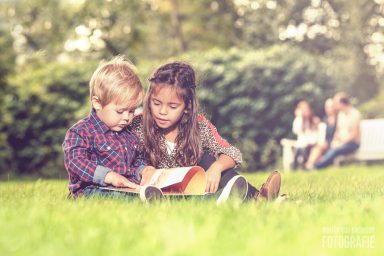 Twee kinderen zitten op het gras en lezen samen een boek in een park.