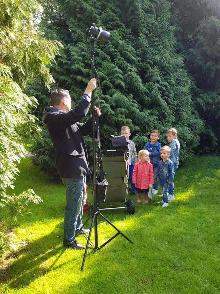 Een fotograaf maakt foto's van vijf kinderen in een groene tuin.