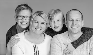 Gezin met twee kinderen, lachend en samen staand, op een neutrale achtergrond.
