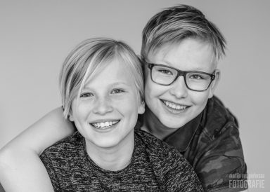 Twee jonge kinderen met blonde haren glimlachen naar de camera.