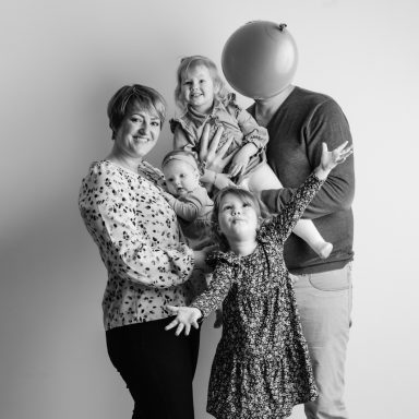 Gezinsfoto met vier kinderen en twee volwassenen, één volwassene houdt een ballon.