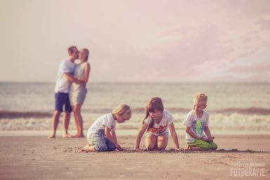 Kinderen spelen op het strand terwijl een stel elkaar omarmt op de achtergrond.