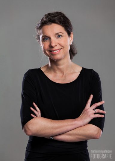 Vrouw met een glimlach, gekruiste armen, draag zwart shirt, neutrale achtergrond.