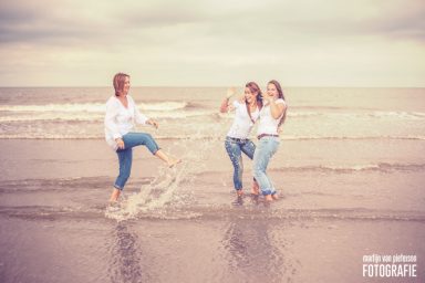 Drie vrouwen lachen en spelen in de branding op het strand.