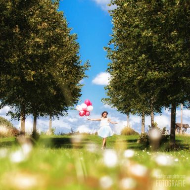 Een meisje in een witte jurk rent met ballonnen door een zonnig grasland.