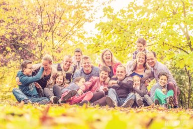 Een grote groep mensen, lachend en zittend op de grond tussen herfstbladeren.