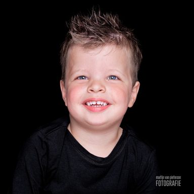 Jong kind met blond haar en een brede glimlach op een zwarte achtergrond.