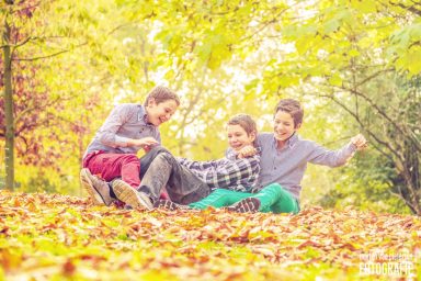 Drie kinderen spelen op een bed van bladeren in een herfstlandschap.