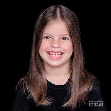 Blond meisje met lange haren en een brede glimlach op een zwarte achtergrond.