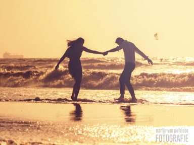 Een silhouet van een stel dat hand in hand over het strand loopt bij zonsondergang.