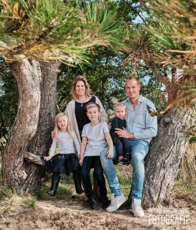 Gezin met twee volwassenen en drie kinderen, zittend tussen bomen in de natuur.