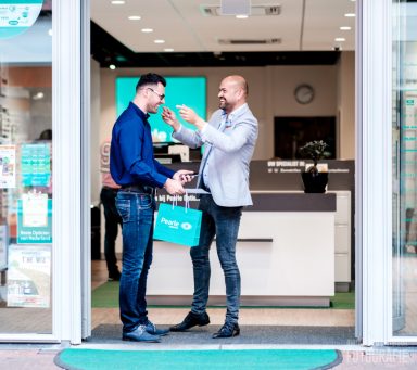 Twee mannen staan in een winkel, één geeft de ander een pakketje.