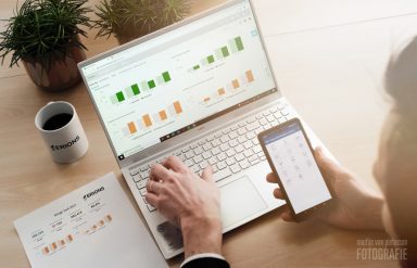 Een persoon werkt op een laptop met grafieken en kijkt tegelijkertijd naar een smartphone.