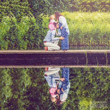 Een stel staat op een oever, terwijl ze elkaar liefdevol aankijken en hun reflectie in het water zien.