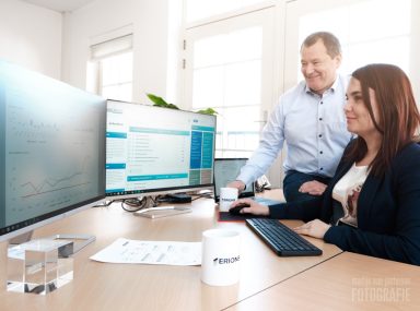 Een man en een vrouw werken samen aan een computer aan een bureau in een kantooromgeving.
