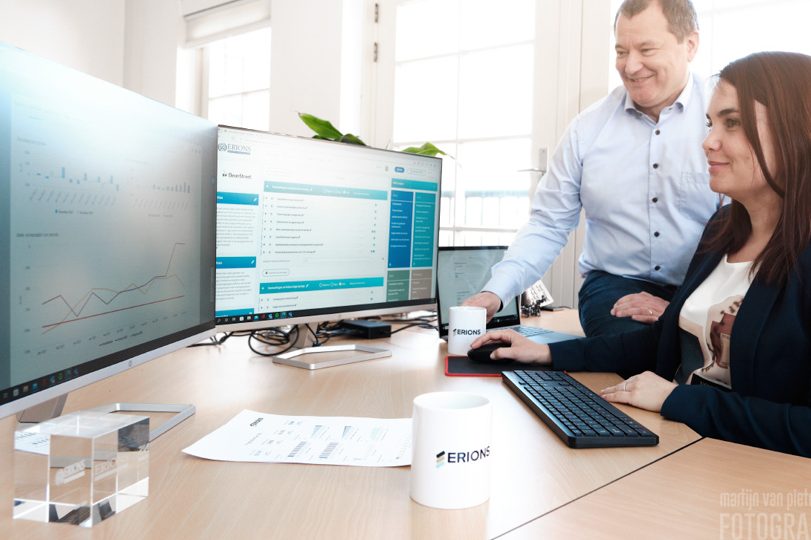 Twee mensen werken samen aan een bureau met computers en aantekeningen.