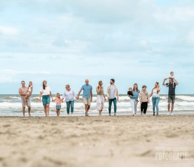 Groep mensen wandelt langs het strand met de zee op de achtergrond.